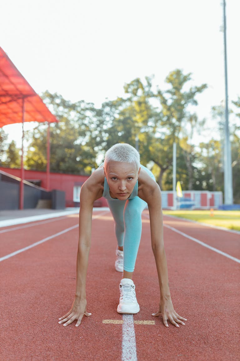 Determined female athlete in focus, ready to sprint on an outdoor track, showcasing fitness and focus.